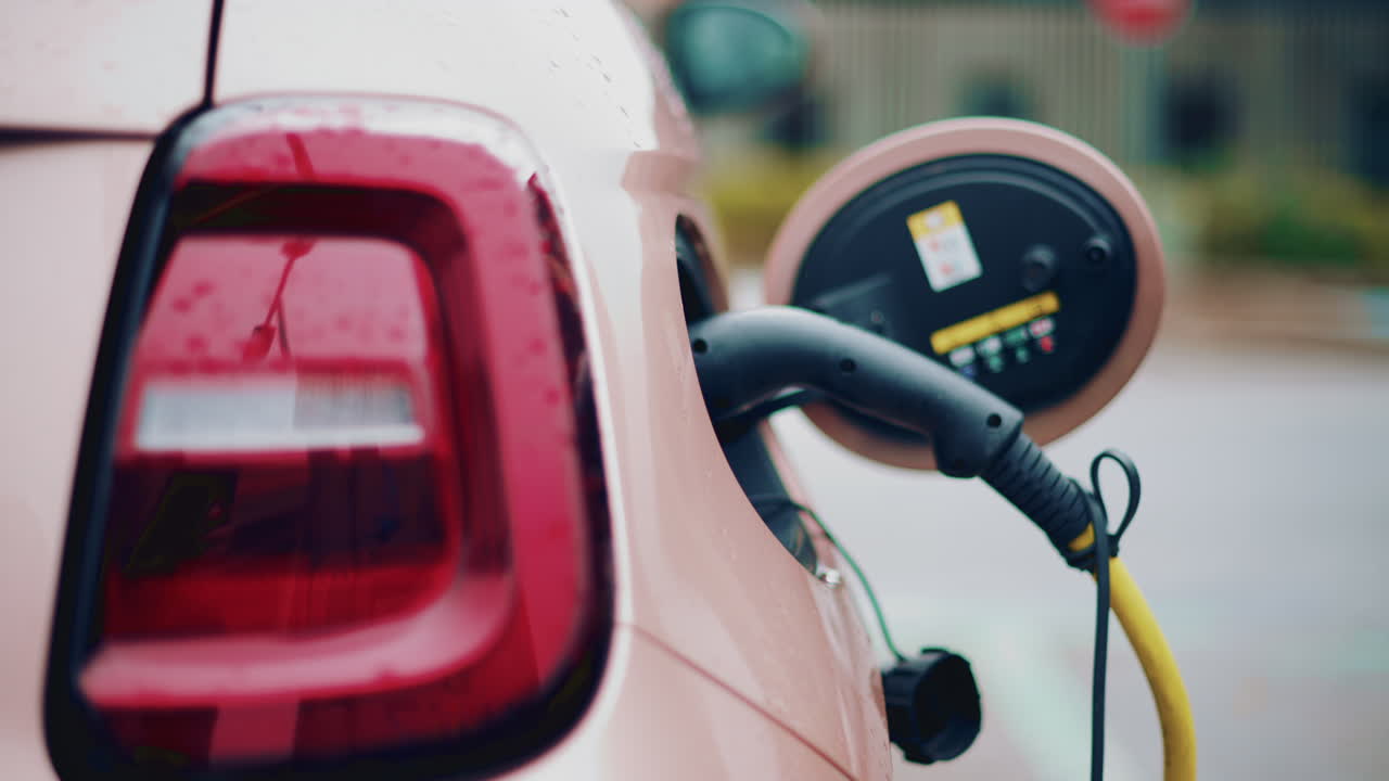 Close up of a pink, electric car charging outdoors under rain