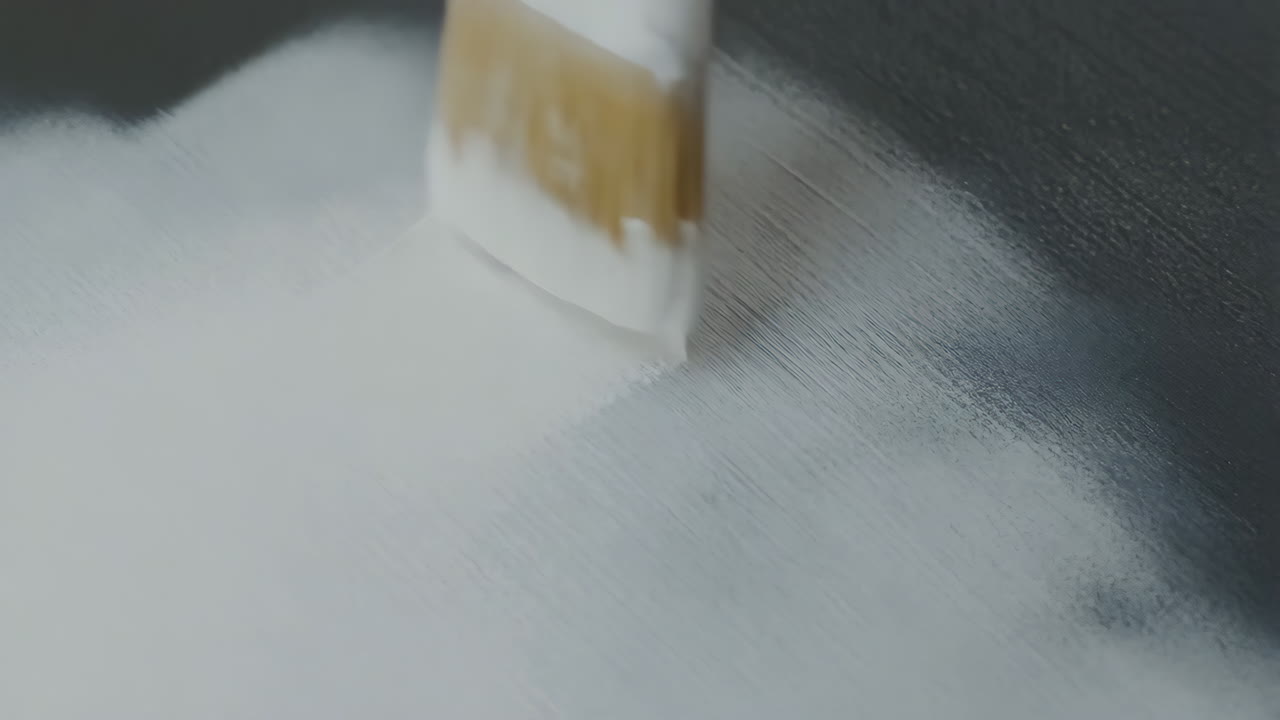 Paintbrush applying white paint to a dark surface