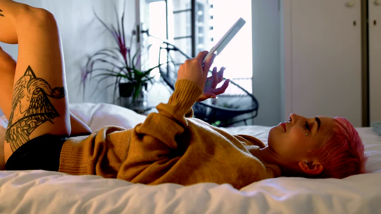 mujer de cabello rosa usando tableta digital en la cama en el dormitorio 4k