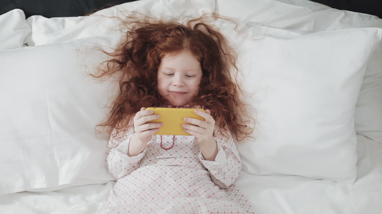Girl with red hair playing with her phone in bed