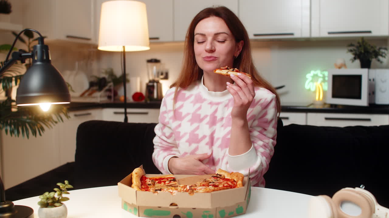 Adult woman eats pizza at night hungry cheat meal breaks diet enjoys secret late snack happy smiles