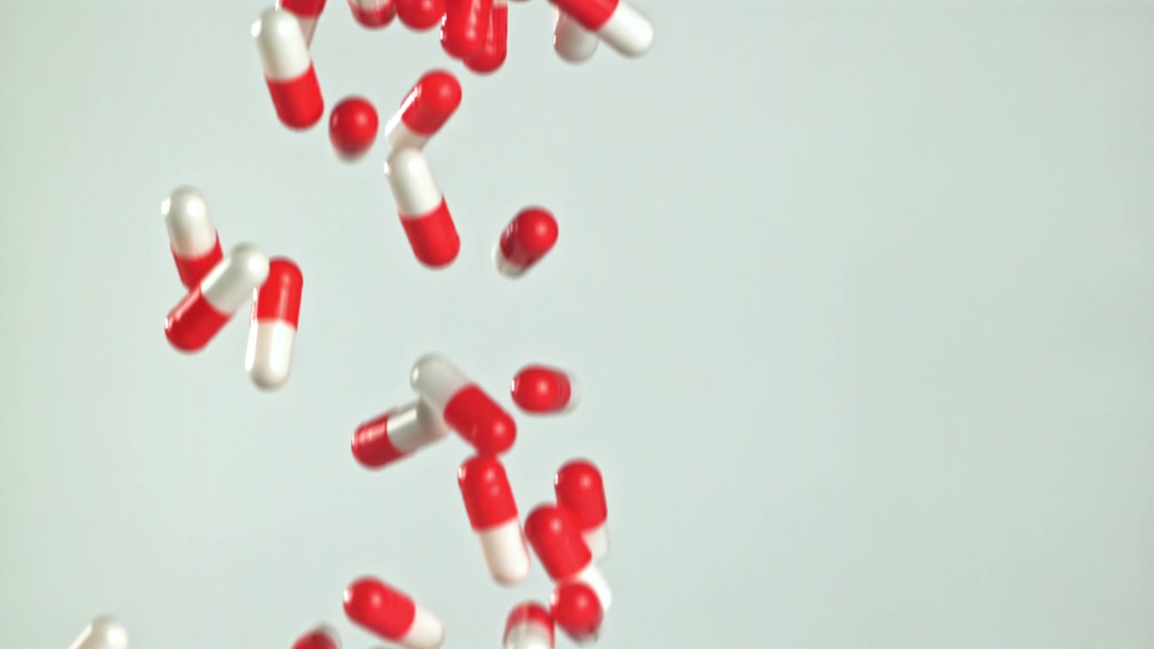 Capsule farmaceutiche rosse e bianche che cadono al rallentatore
