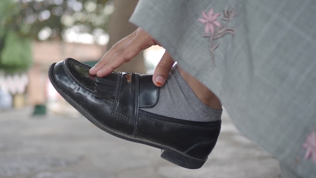 A person's hand adjusting a black loafer shoe