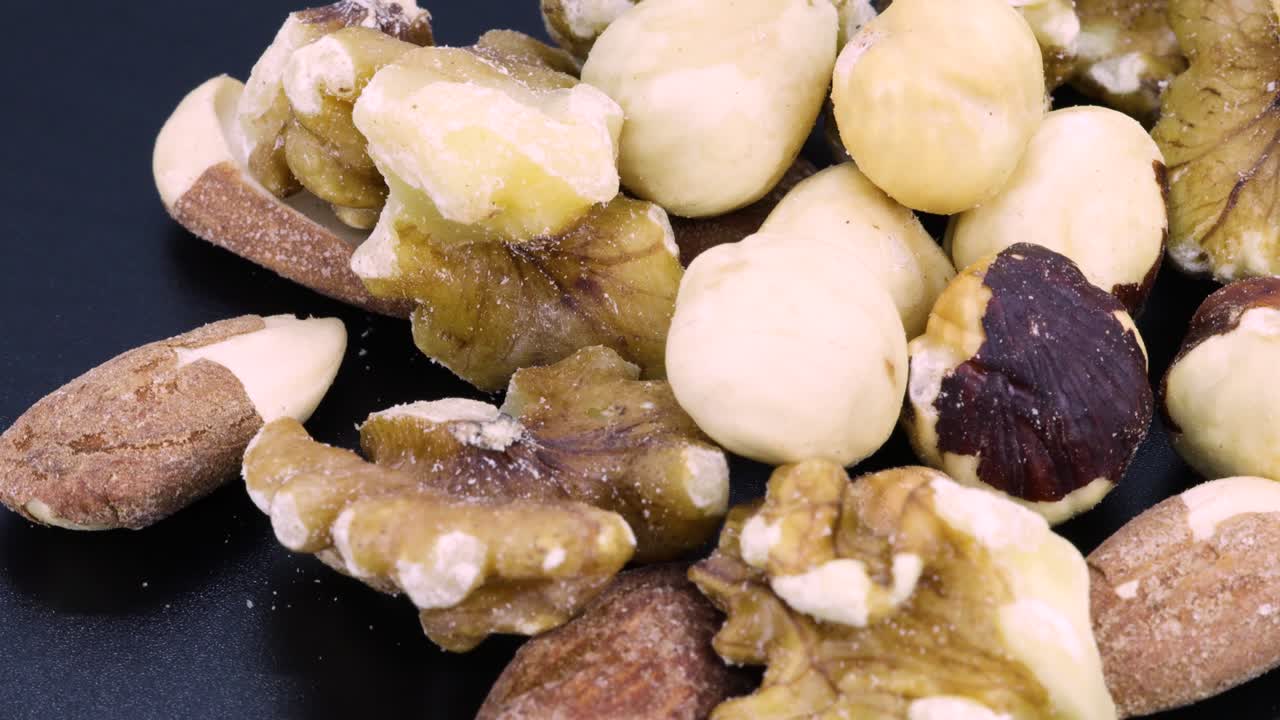 Ripresa dettagliata ravvicinata e rotante di un mix energetico: mix macro di noci, noci, mandorle e nocciole, ripresa ravvicinata che ruota su uno sfondo nero