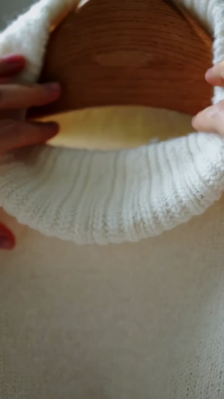 Vertical video: Entering frame hands smoothing knit sweater collar in room showing detail, hanger