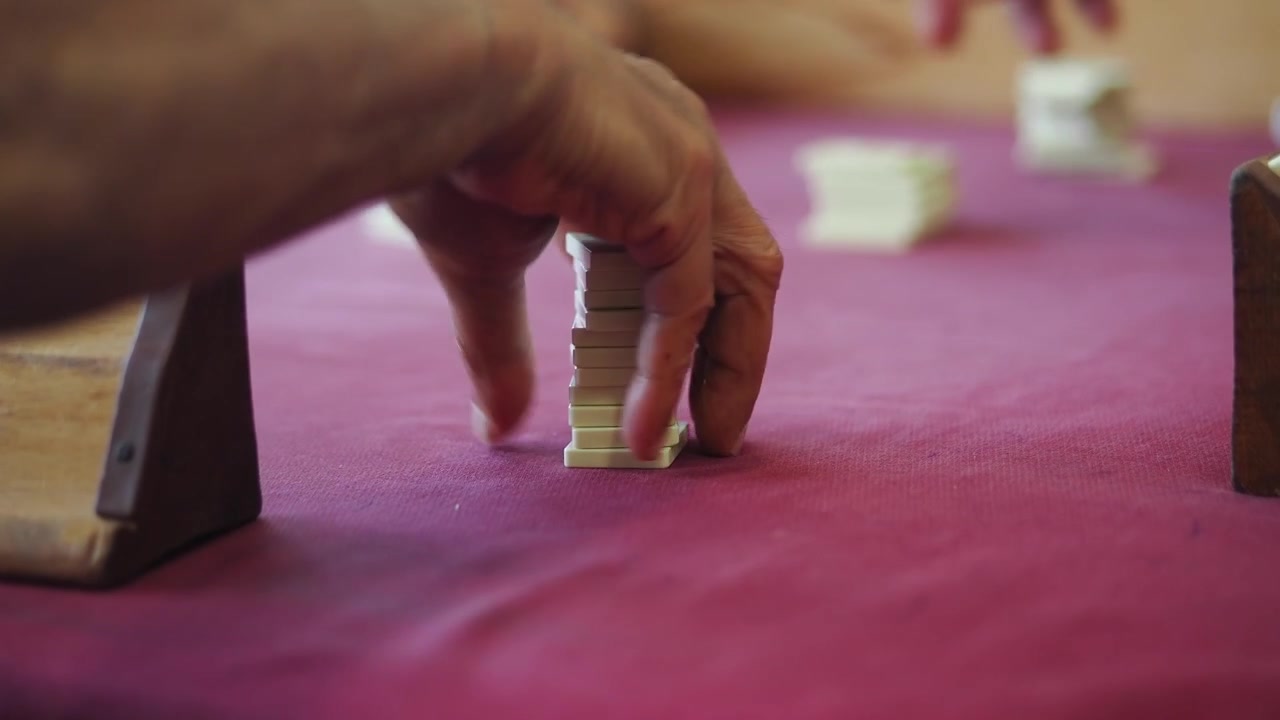 Senior Person Playing Rummy Tile Game on Red Table