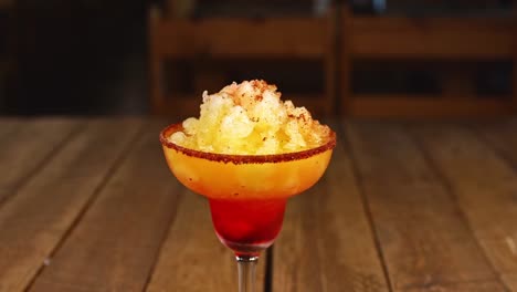 Cóctel-Con-Helado-De-Piña,-Chile-En-Polvo-Y-Vodka-Sobre-Una-Mesa-De-Madera,-La-Mano-Arroja-Una-Cereza-Sobre-El-Cóctel