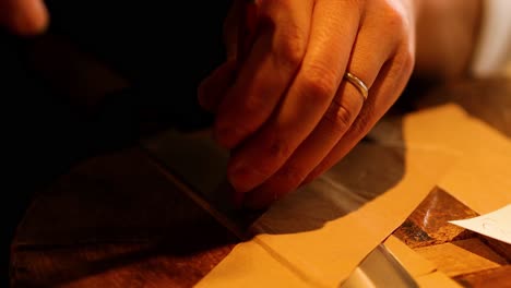 close-up of hands using a red wax stick to work on paper, showcasing detailed craftsmanship.