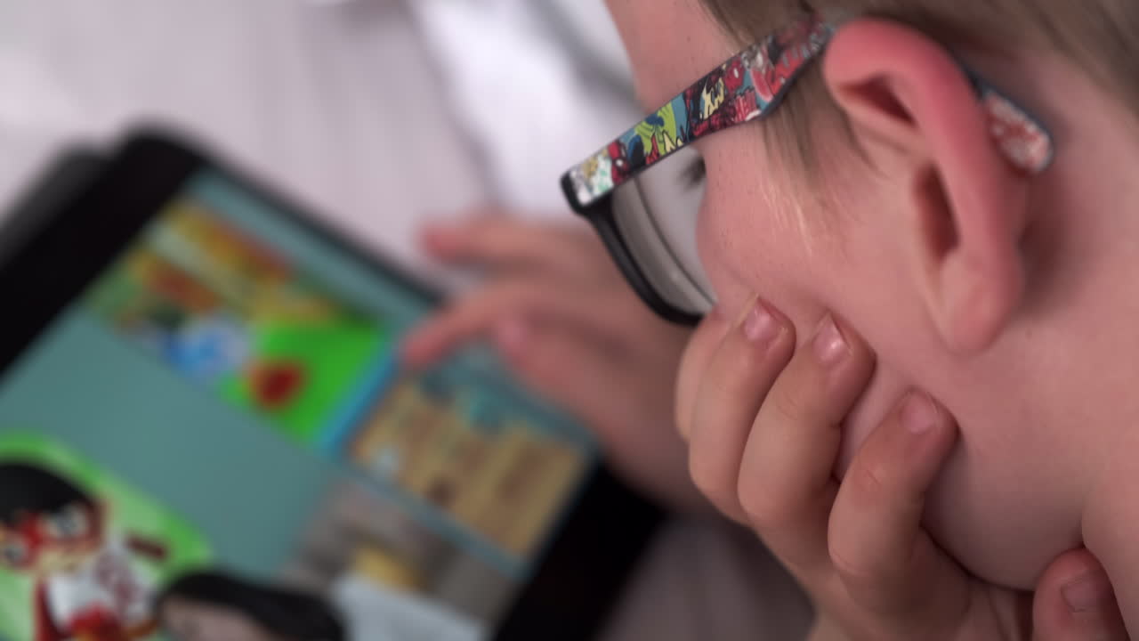 침대에 누워 컴퓨터 태블릿을 읽는 6세 소년