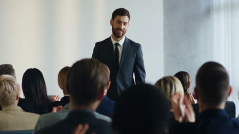 caucasian businessman making a speech at a conference and pointing at someone from the audience, then approeaches to a woman