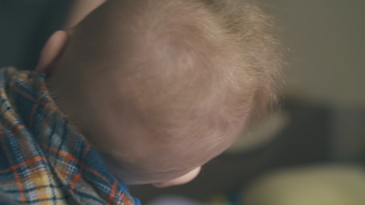 blond baby in bright shirt plays with spoon on soft bed