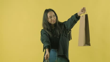 joven hermosa con bolsas de compras en el fondo amarillo