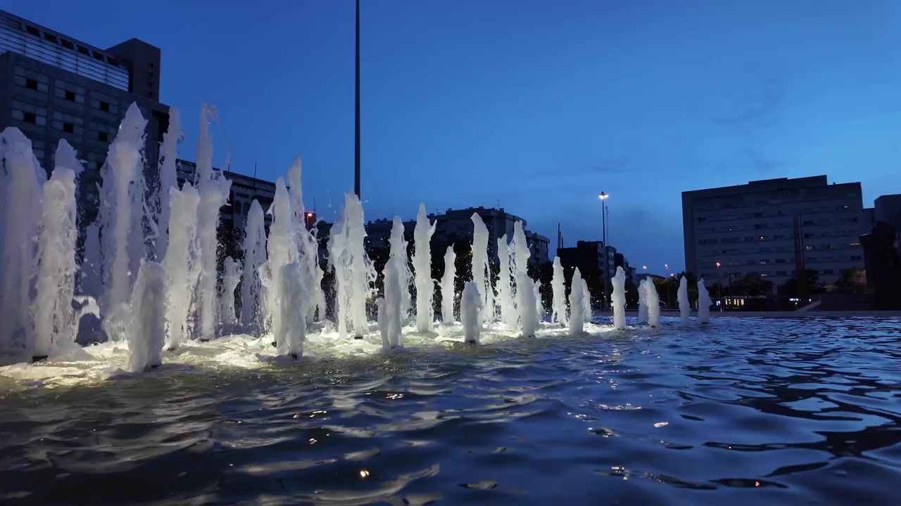 Escena nocturna: Fuente de agua iluminada con edificio arquitectónico en el centro de la ciudad de Maia.
