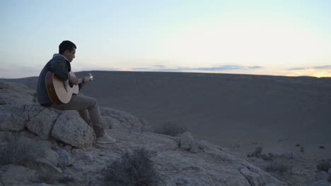 un joven músico toca una melodía durante la puesta de sol en el desierto