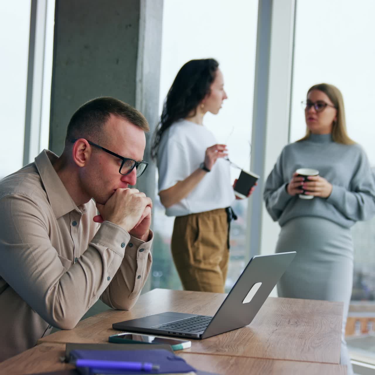 Male employee concentrated on laptop screen. Problem solving at work. Female coworker chat and drink coffee at backdrop