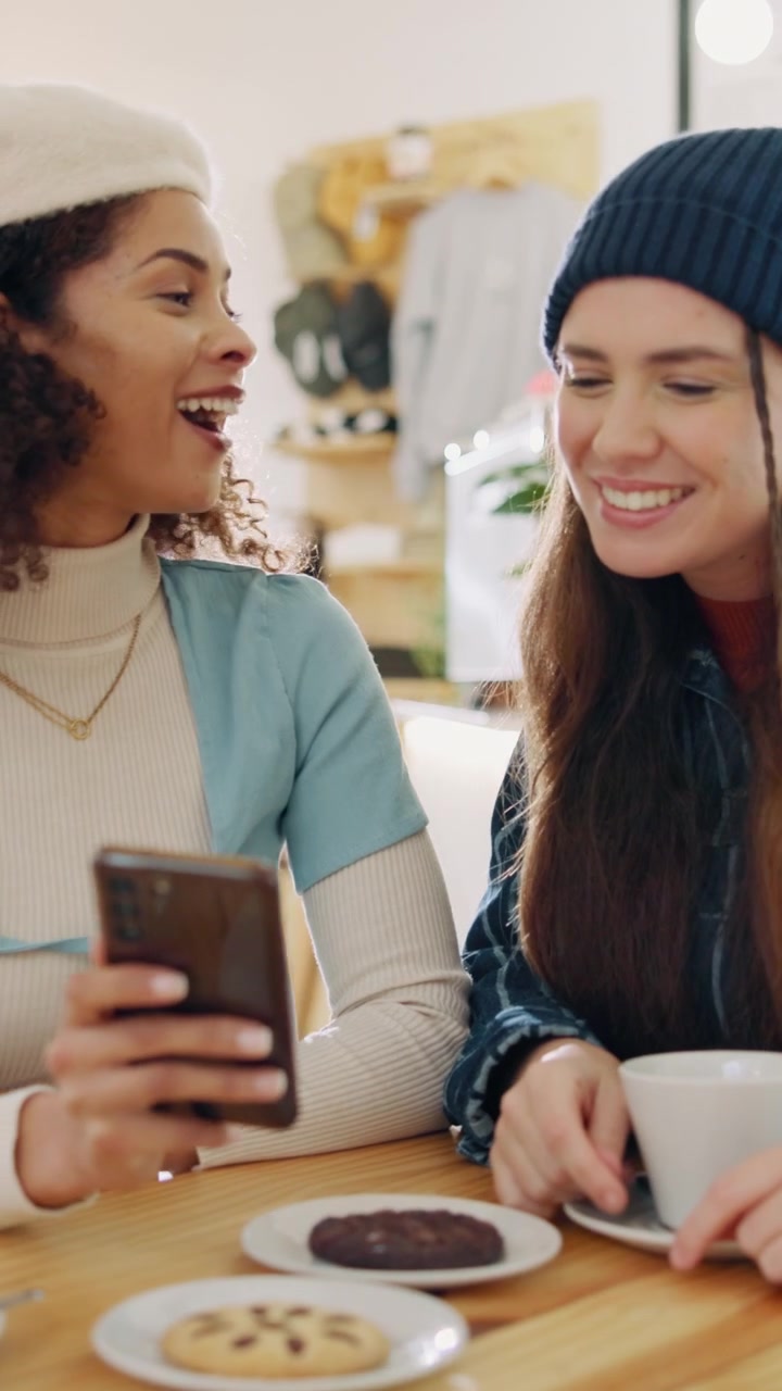 Dos mujeres jóvenes riendo y usando un smartphone en una cafetería