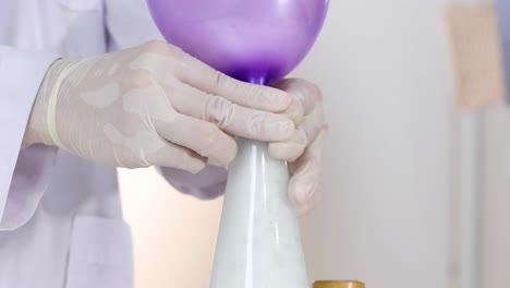 a purple balloon inflates as a white liquid reacts inside a bottle, handled by gloved hands.