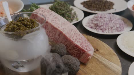 a panning shot reveals various ingredients such as mozzarella, tomatoes, onions, capers, arugula, all centered around caviar on dry ice, creating a captivating effect