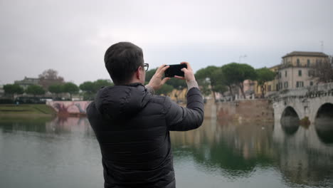 man taking photo of a city river and bridge