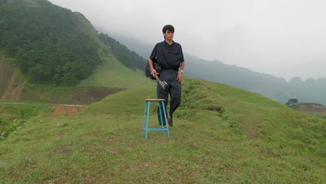 Musician-wearing-black-with-guitar-walks-up-to-stool-and-sits