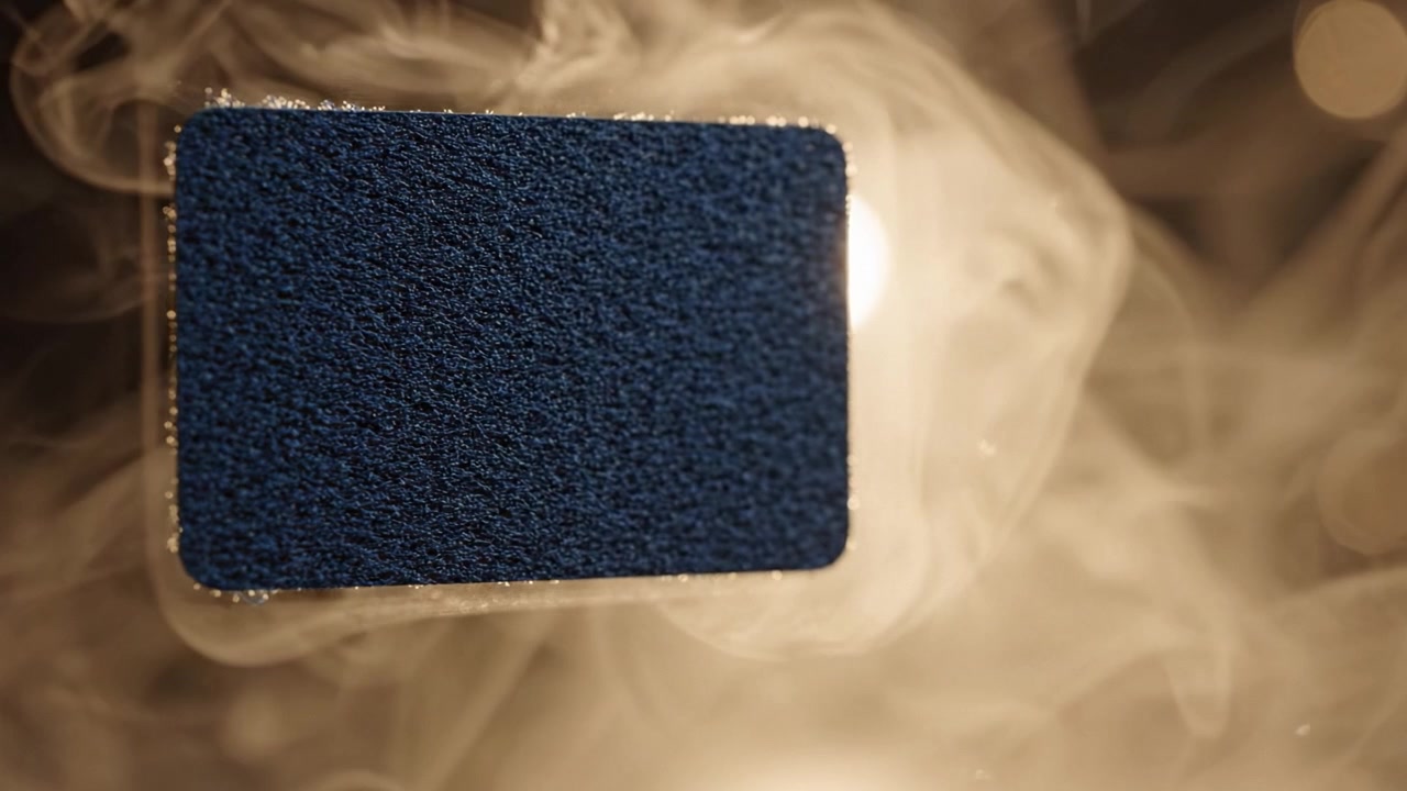 A close-up view of a textured blue surface surrounded by ethereal smoke, creating a striking visual contrast in an artistic and atmospheric setting.