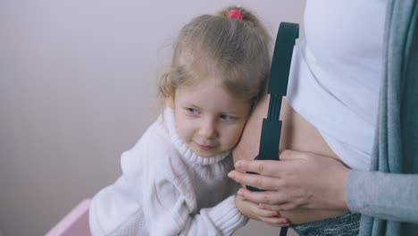funny girl puts black headphones on pregnant mom belly