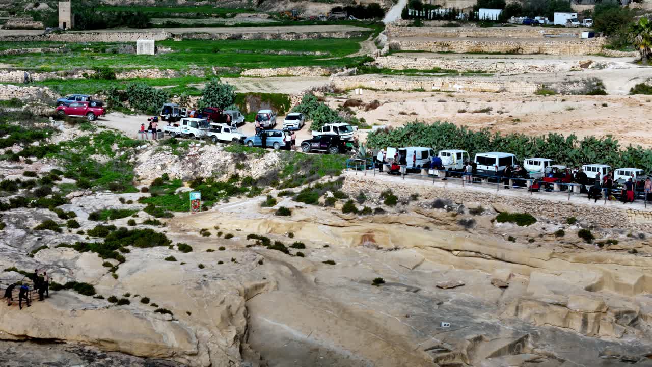 Un vivace gruppo di veicoli da avventura è parcheggiato in cima alle scogliere calcaree assolate di Gozo durante un luminoso pomeriggio primaverile sotto un cielo azzurro terso, caratterizzato da calde tonalità terrose da una vista dall'alto