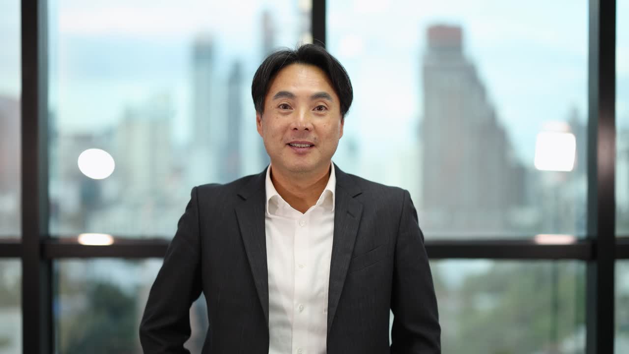 Smiling Asian businessman in suit celebrates achievement with raised fists, natural daylight, static camera