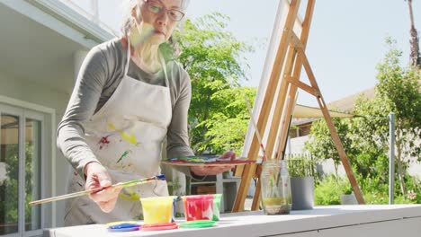 Asiatische-ältere-Frau-Trägt-Schürze-Und-Malt-An-Einem-Sonnigen-Tag-Im-Garten