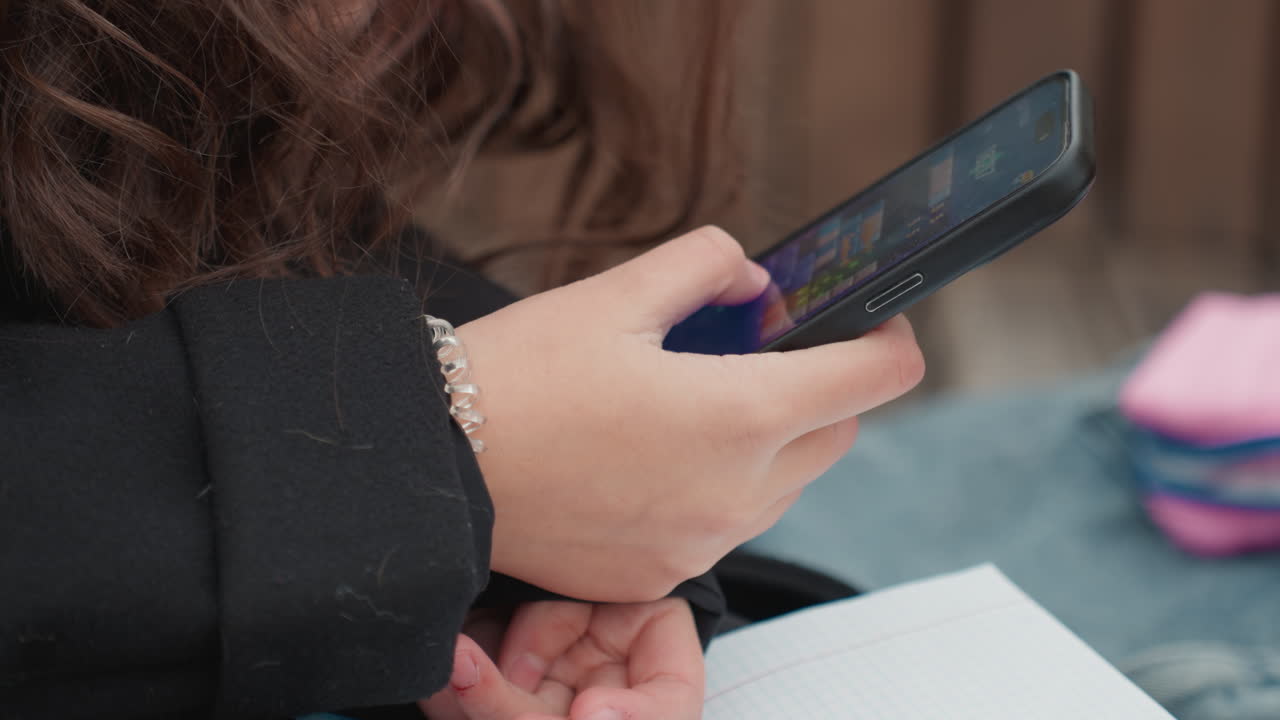 Uno studente controlla i messaggi durante la pausa. Persona che utilizza il telefono tra materiali di studio all'aperto. Giovane studente interagisce con un dispositivo mobile all'aperto, circondato da oggetti di studio e luce naturale.