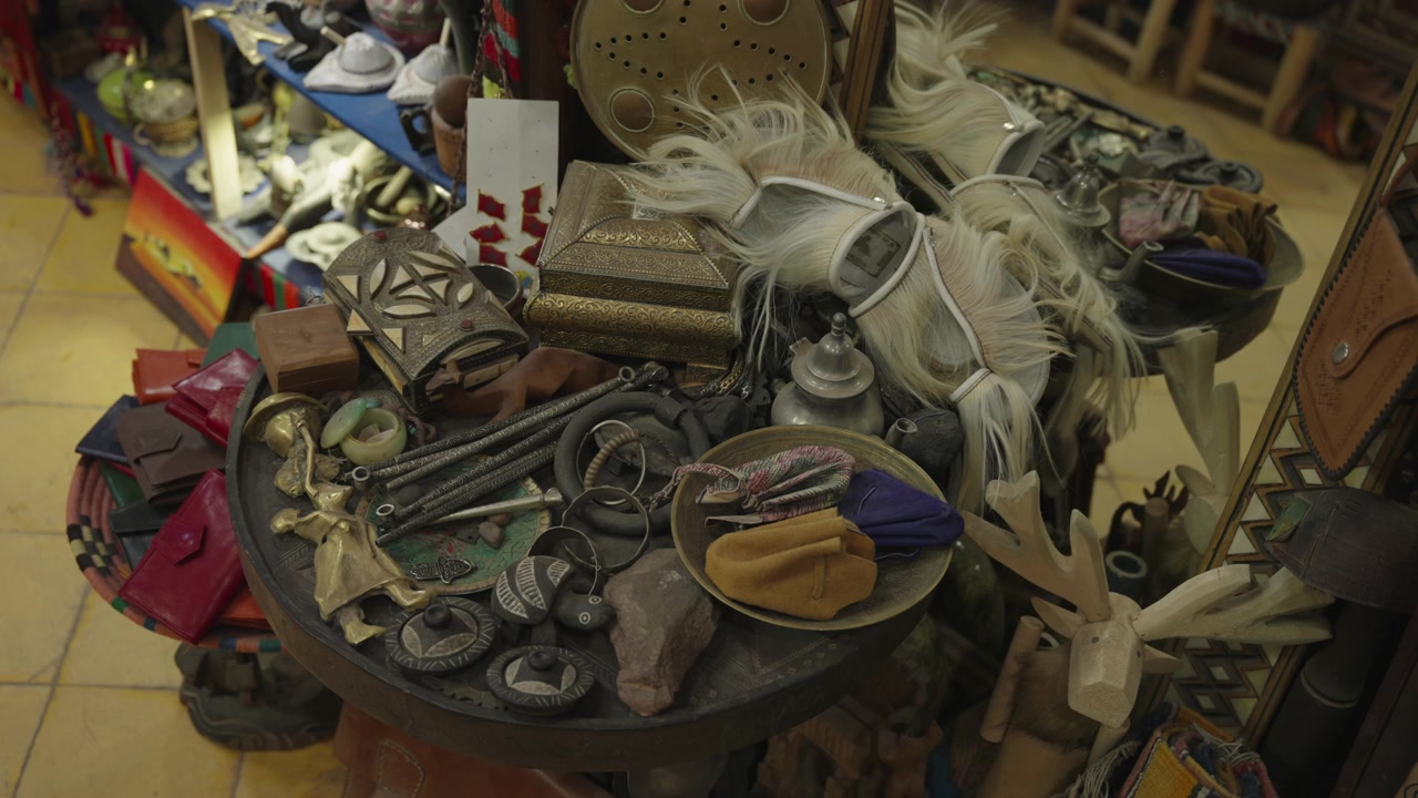 Tavolo espositivo ricolmo di artigianato tradizionale marocchino, oggetti in metallo, gioielli, piume e oggetti d'antiquariato all'interno di un negozio di souvenir locale.