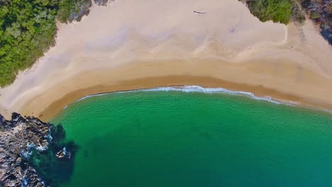 Aufsteigender-Blick-Von-Oben-Auf-Klare-Smaragdgrüne-Wellen,-Die-Eine-Leere-Weiße-Sandstrandbucht-Umspülen