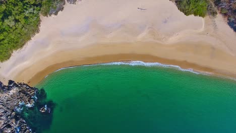 vista aérea ascendente de claras olas esmeralda que lamen una cala vacía de arena blanca