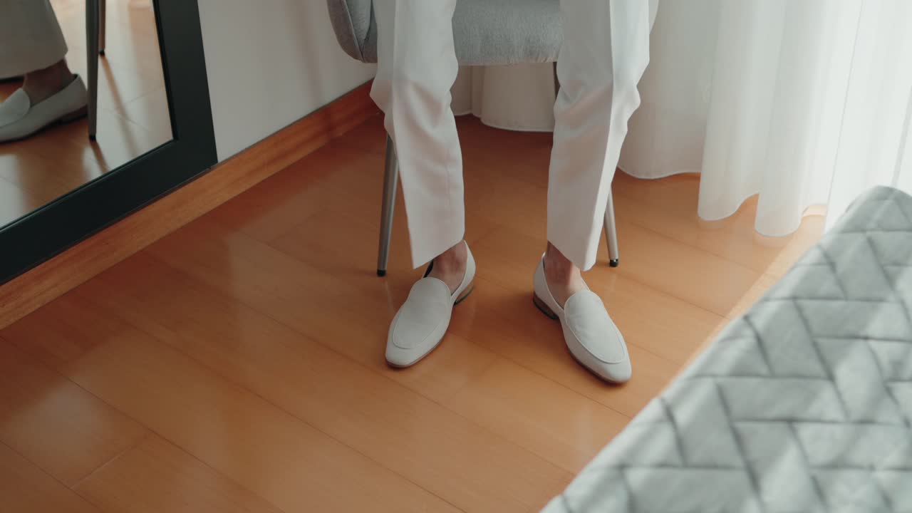 색 의복 을 입은 신랑 은 다리 를 고 앉아 결혼식 전 에 집 안 에서 우아 한 로퍼 를 전시 하고 있다