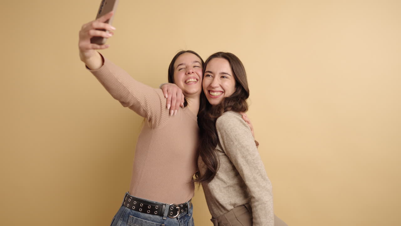 Friends posing playfully for a selfie against a beige background