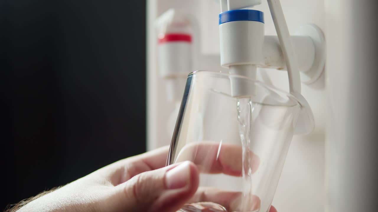 Primo piano di una mano che riempie un bicchiere d'acqua da un dispenser