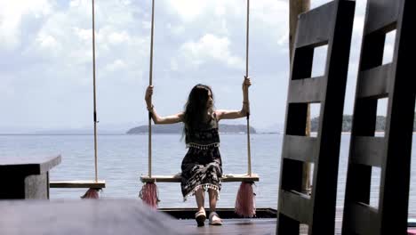 beautiful girl is riding on a swing against the sea in a cafe on the pier