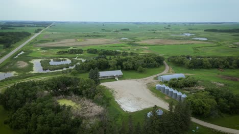 Filmische-Luftdrohnenumlaufbahn-Um-Weideland,-Landwirtschaftsdemonstration,-Rinderfarmhaus,-Erntebehälter-Und-Natur,-Präriefeldlandschaft-Mit-Highway-Ufersee