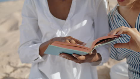 closeup hands open book pointing page beach picnic. relaxed girls read romance