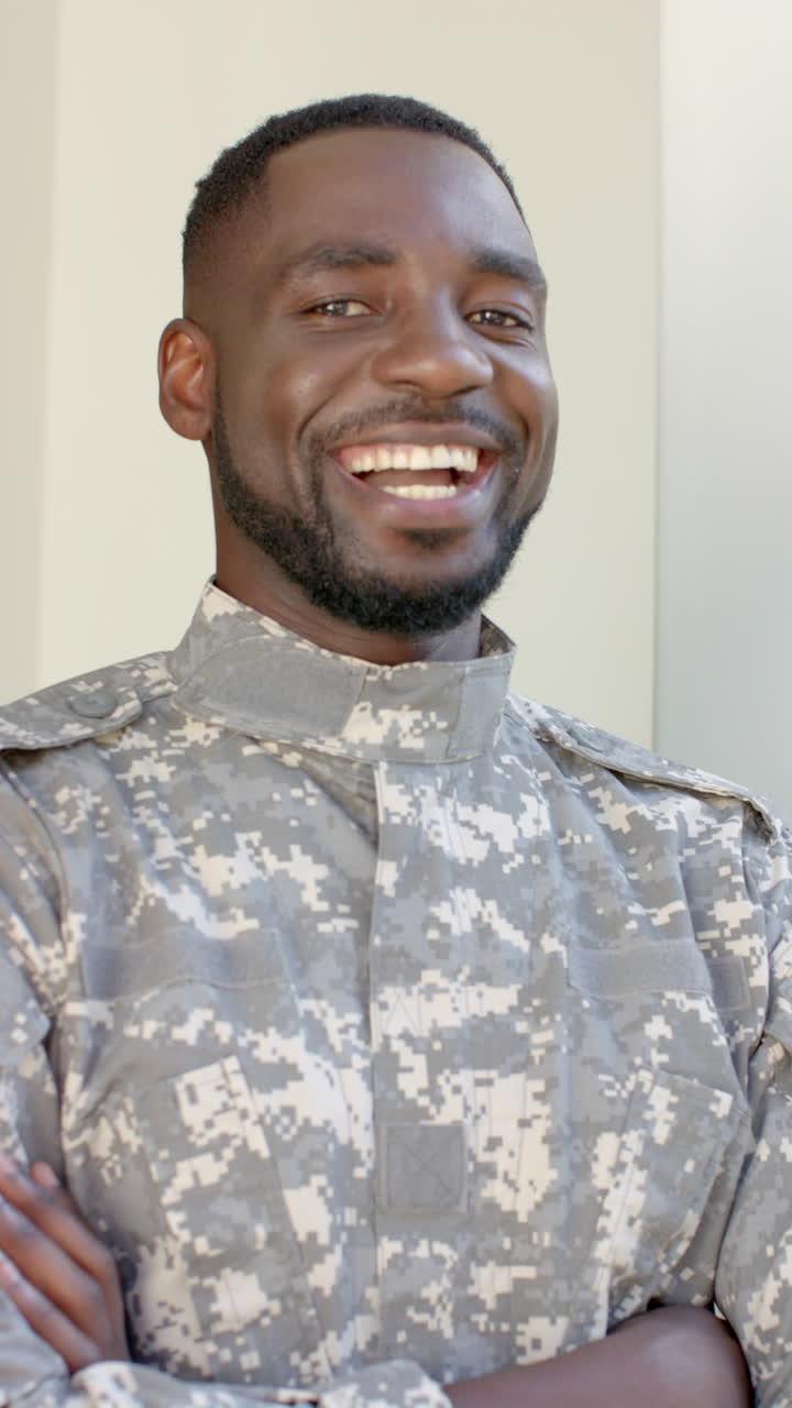 Vertical video: Smiling male soldier in uniform standing with arms crossed indoors