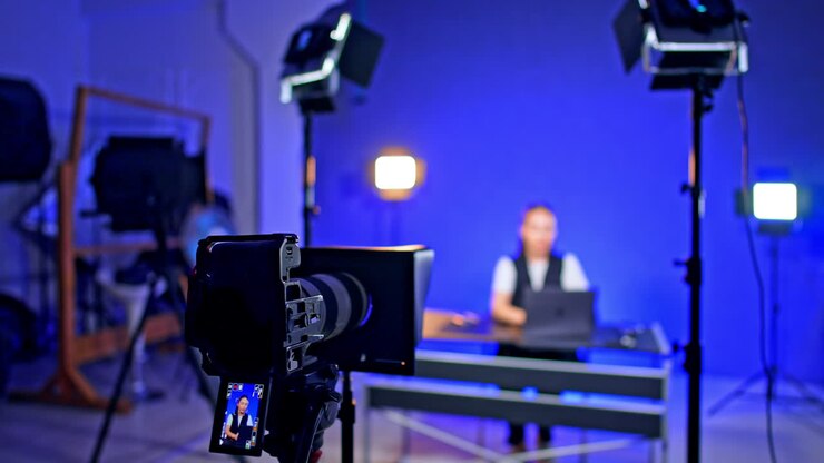 Configurazione studio video. Una persona è seduta a una scrivania con un laptop in uno studio ben illuminato, preparandosi per una sessione di registrazione video