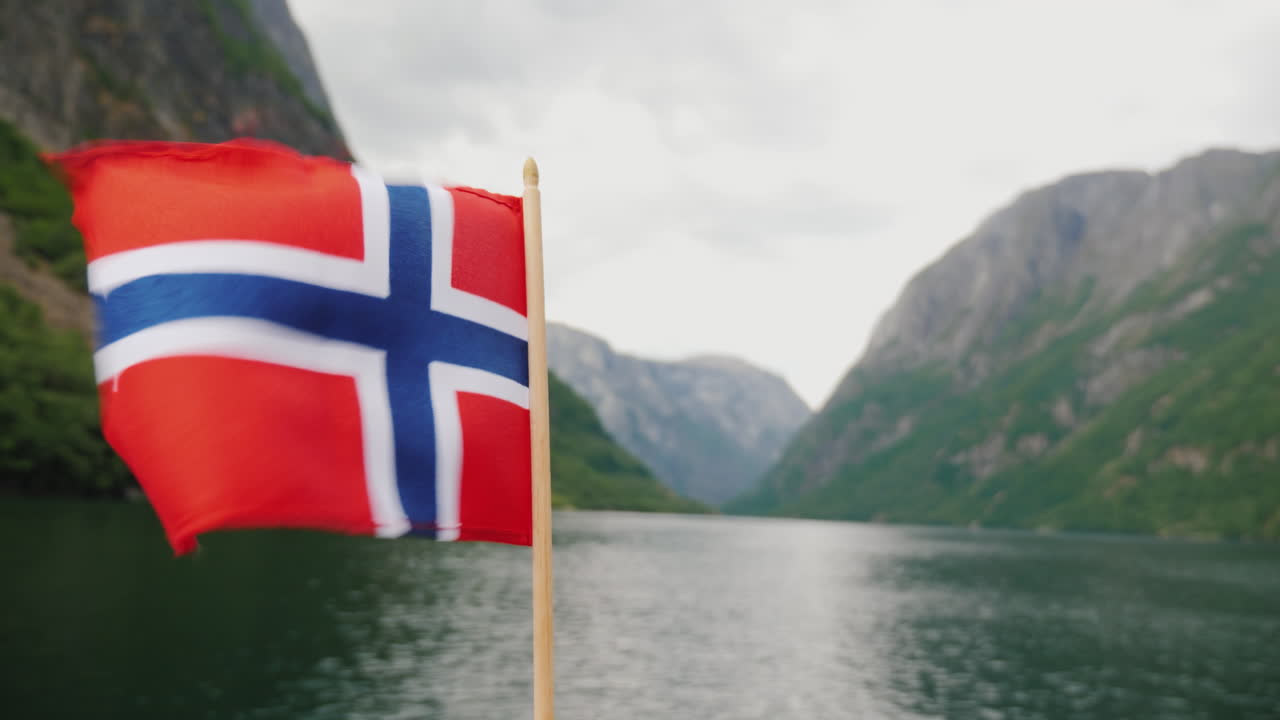 la bandera noruega ondea en el viento contra el telón de fondo de un majestuoso crucero por los fiordos o