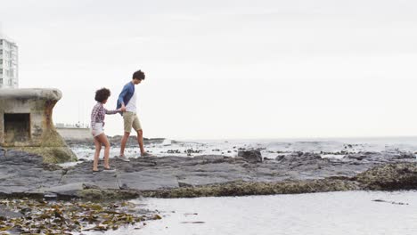 african american couple holding hands walking on the rocks near the sea