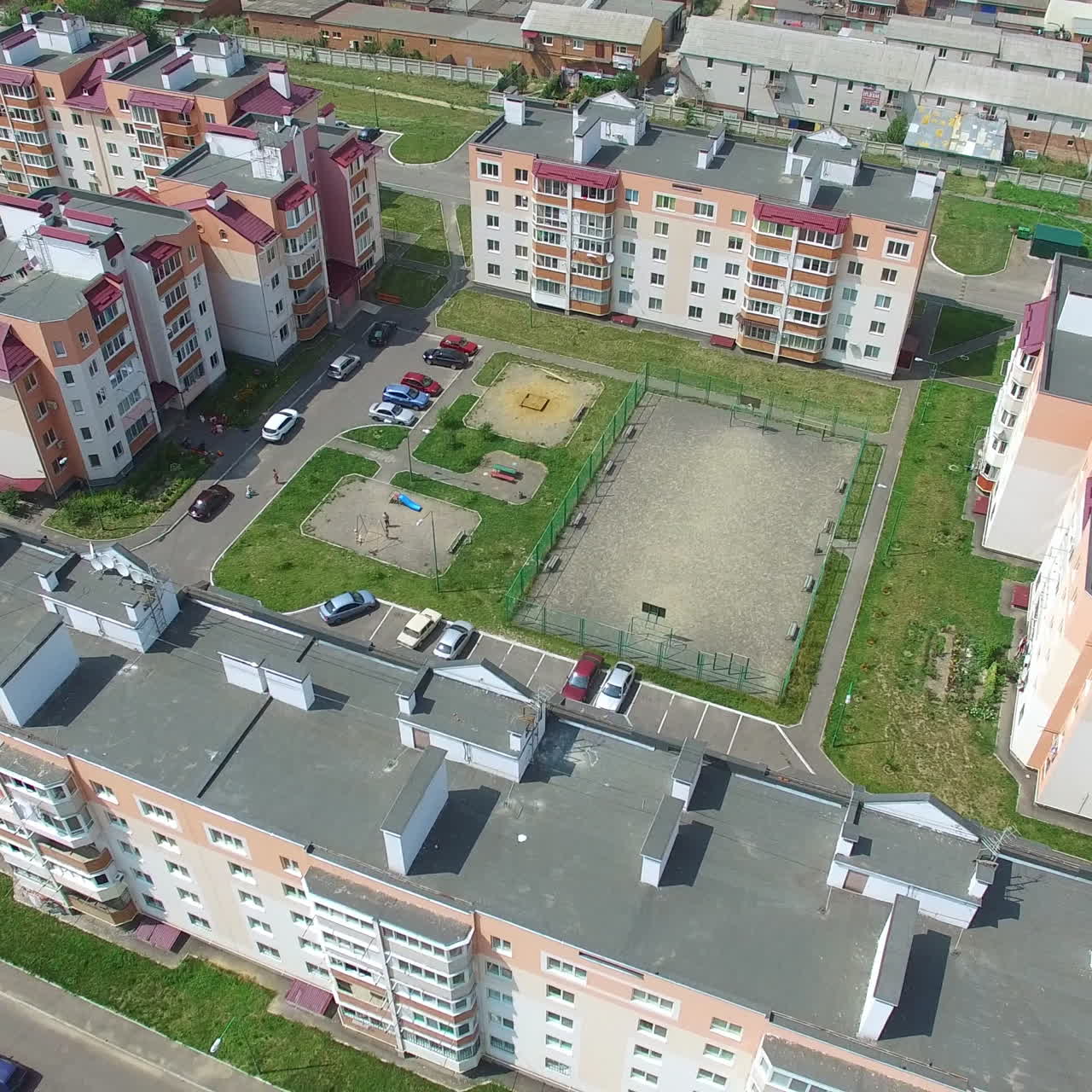 Beautiful view of newly built complex with cars in the streets and green grass near the buildings. Camera moves back. Aerial view