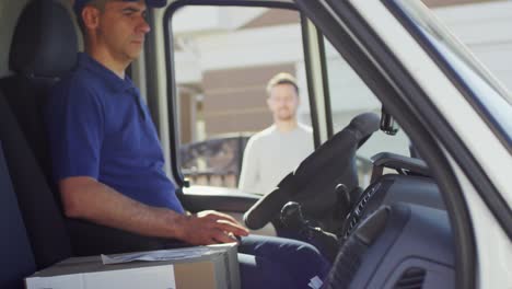 male postal service courier sitting in mail van shaking hands with client and delivering him a package