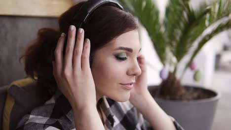 A-brunette-girl-with-a-beautiful-make-up,-puts-on-headphones-and-listens-with-pleasure-to-her-favorite-music.-Gestures-with-his-hands.-Close-up