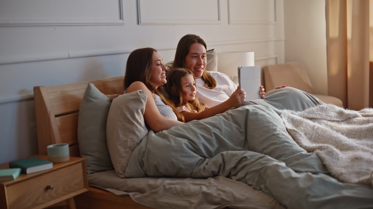 Happy family watching video on tablet computer lying under blanket together