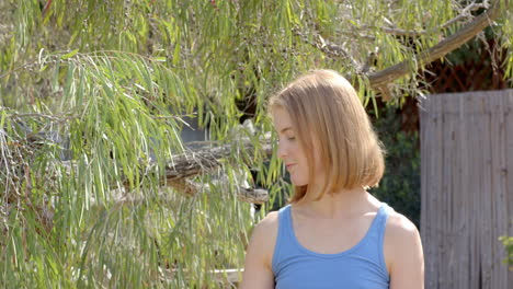 woman in blue tank top standing outdoors, surrounded by lush greenery, copy space