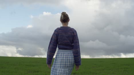 una mujer joven caminando por un campo verde en un día nublado y malhumorado, cámara lenta