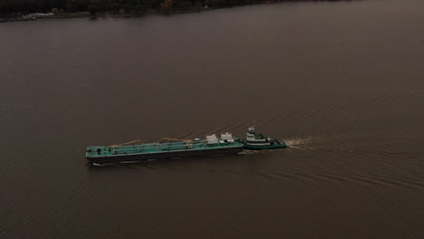 aerial shot over a turqiuse colored barge - tugboat on the hudson river on a cloudy day in beacon, ny